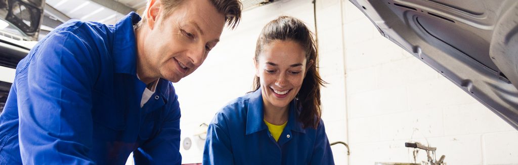 Apprentice mechanic working on vehicle with colleague